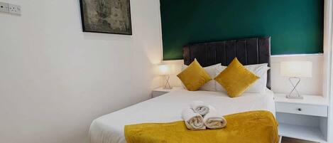 A modern bedroom with a bed, bedside tables, and a green accent wall.