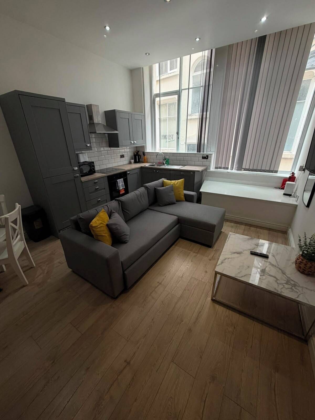 A modern kitchen with grey cabinets, a built-in microwave, and a window with curtains.