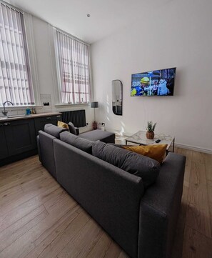 A modern living room with a grey sofa, a small table with a plant, and a television mounted on the wall. - Sweeting Street Apartment (Liverpool)