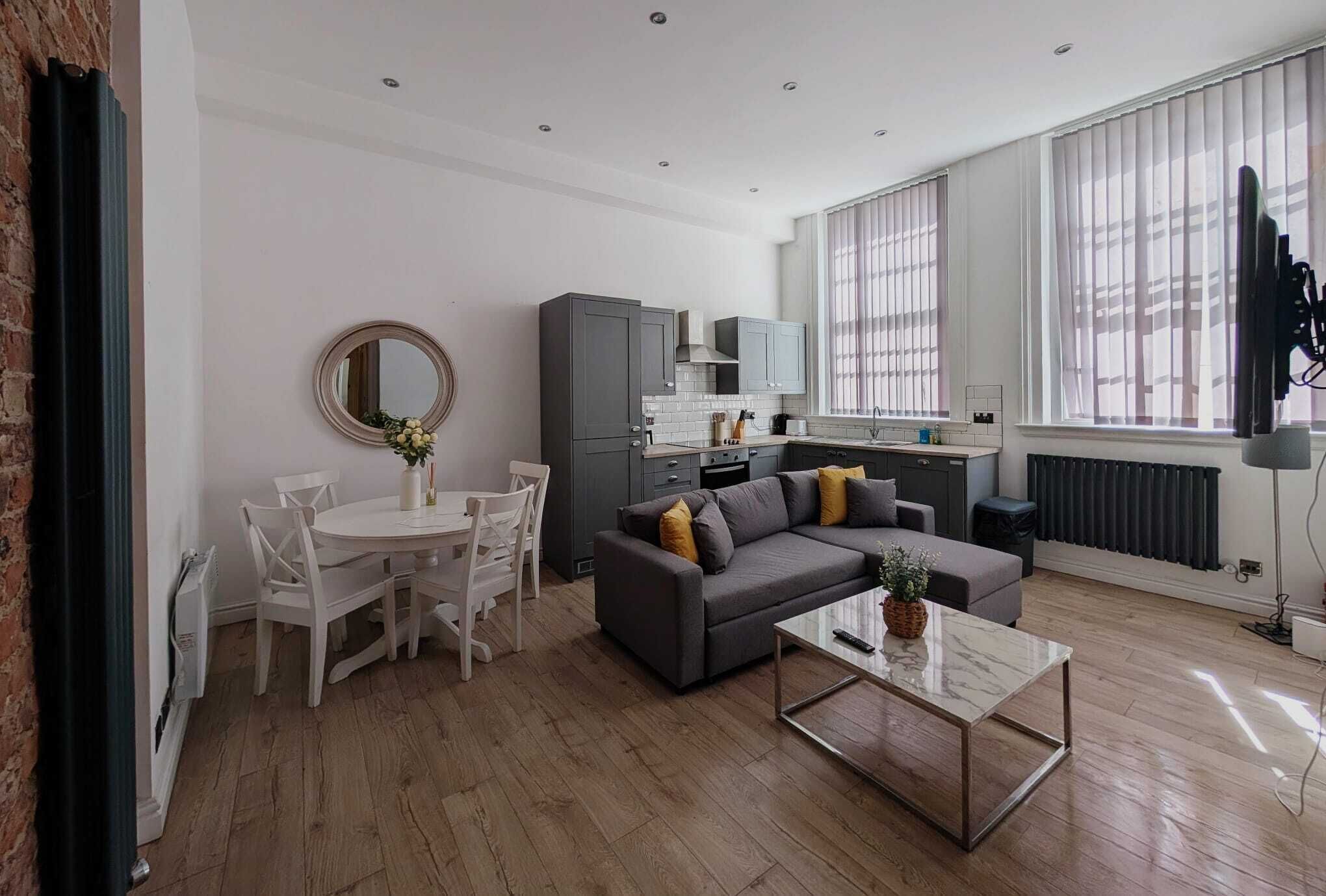 A modern living room with a grey sofa, a coffee table, and a dining area with a white table and chairs.