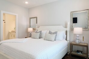 A neatly made bed with a white duvet and several pillows, a bedside table with a lamp, and a mirror on the wall. - "Grove Getaway" by OVR (Oxford)