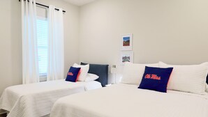 Ett hotellrum med två sängar, var och en med ett vitt, vadderat sängöverkast och blå kuddar med texten ”Ole Miss”.