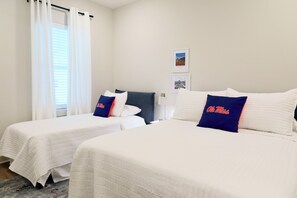 Ein Hotelzimmer mit zwei Betten, jeweils mit weiß gestopfter Bettdecke und blauen Kissen mit dem Aufdruck 'Ole Miss'.