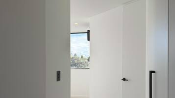 A hallway with white walls, a carpeted floor, and a door leading to a room with a window.