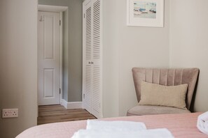 A bedroom with a bed, a chair, a wardrobe, and a framed picture on the wall. - Stunning Garden Flat in Heart of Cheltenham (Cheltenham)