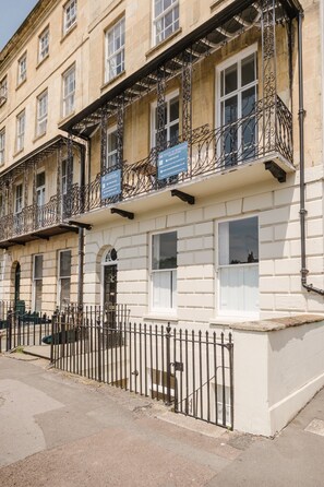 A building with multiple windows, a balcony with wrought iron railings, and a gated entrance. - Stunning Garden Flat in Heart of Cheltenham (Cheltenham)