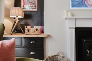 A room with a fireplace, a bookshelf, a lamp, and a wicker basket. - Stunning Garden Flat in Heart of Cheltenham (Cheltenham)