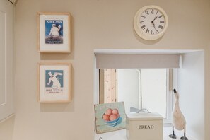 A kitchen with a wall clock, framed posters, a bread box, and a decorative bird. - Stunning Garden Flat in Heart of Cheltenham (Cheltenham)