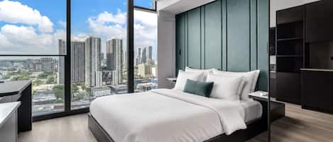 Une chambre moderne avec un grand lit, un bureau et une vue sur le paysage urbain grâce à de grandes fenêtres du sol au plafond.