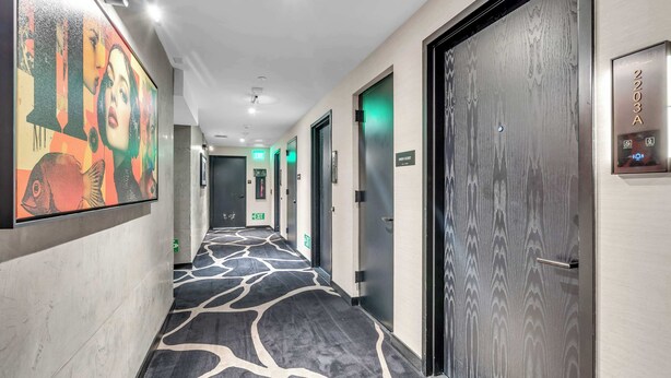A hotel corridor with a patterned carpet, doors, and an exit sign. - Highrise Condo & Amenities (Miami)