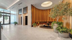 A spacious lobby with a modern design, featuring a seating area with a sofa and a coffee table, and several potted plants. - Highrise Condo & Amenities (Miami)