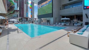 A rooftop pool area with lounge chairs and a large screen displaying a sports event. - Highrise Condo & Amenities (Miami)