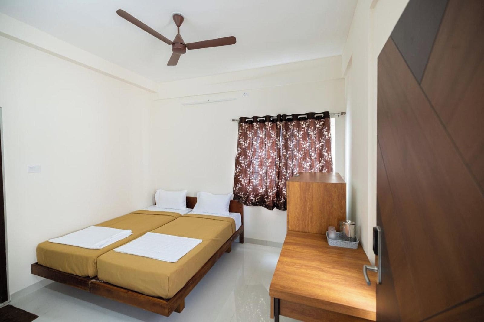 Une chambre avec un lit, un bureau, un ventilateur de plafond et une fenêtre avec des rideaux.