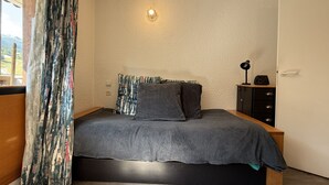 A bedroom with a bed, a nightstand, a lamp, and a view of the outdoors. - Studio apartment at the base of the ski lifts, in the center of the resort (Modane)