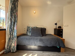 A bedroom with a bed, a nightstand, a lamp, and a view of the outdoors. - Studio apartment at the base of the ski lifts, in the center of the resort (Modane)