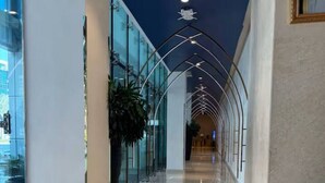 Un couloir doté d’un sol réfléchissant, de murs en verre et d’un plafond orné d’un luminaire aux formes géométriques.