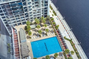 A high-rise building with a rooftop pool surrounded by palm trees and lounge chairs. - Canal View Studio | Balcony + Sofa Bed (Dubai)