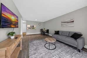 A modern living room with a grey sofa, a round coffee table, and a TV mounted on the wall. - Stylish Furnished Retreat with Modern Comforts (Tamarac)