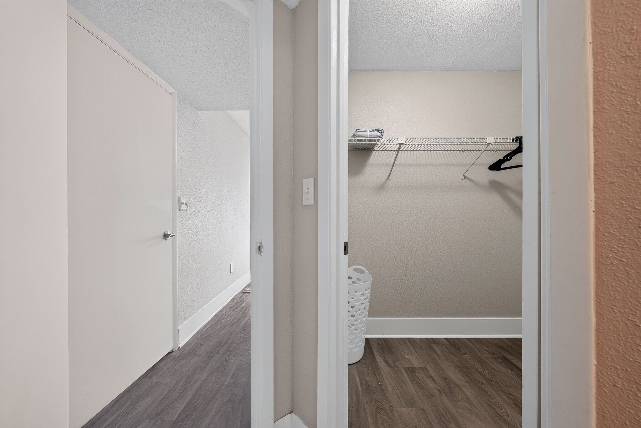 A hallway with a door on the left, a laundry area with a drying rack on the right, and a white laundry basket.