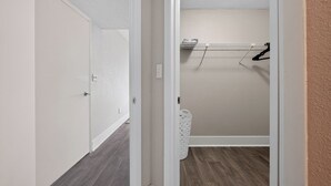 A hallway with a door on the left, a laundry area with a drying rack on the right, and a white laundry basket. - Stylish Furnished Retreat with Modern Comforts (Tamarac)