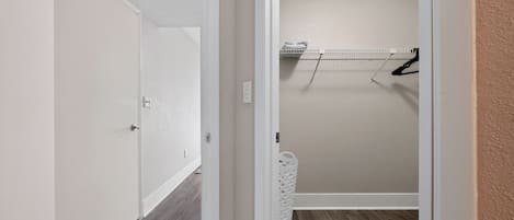 Um corredor com uma porta à esquerda, uma área de lavanderia com um varal à direita e um cesto de roupa branco.