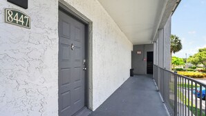 A building with a white exterior, a dark grey door, and a balcony with a metal railing. - Stylish Furnished Retreat with Modern Comforts (Tamarac)