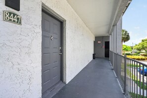 A building with a white exterior, a dark grey door, and a balcony with a metal railing. - Stylish Furnished Retreat with Modern Comforts (Tamarac)