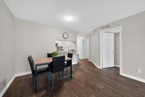 A modern kitchen with white cabinets, a clock, and a dining area with a wooden table and chairs. - Comfortable Modern Home with Resort Amenities (Tamarac)