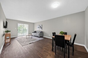 A spacious living room with a grey couch, a dining table with chairs, and a wooden floor. - Comfortable Modern Home with Resort Amenities (Tamarac)