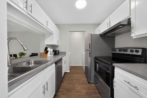 A modern kitchen with stainless steel appliances, white cabinetry, and a wooden floor. - Comfortable Modern Home with Resort Amenities (Tamarac)