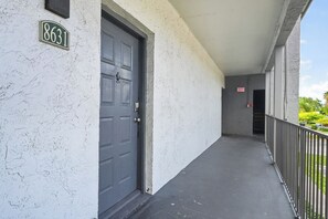 A building exterior with a white textured wall, a black door, and a balcony with a metal railing. - Cozy Contemporary Retreat with Great Amenities (Tamarac)