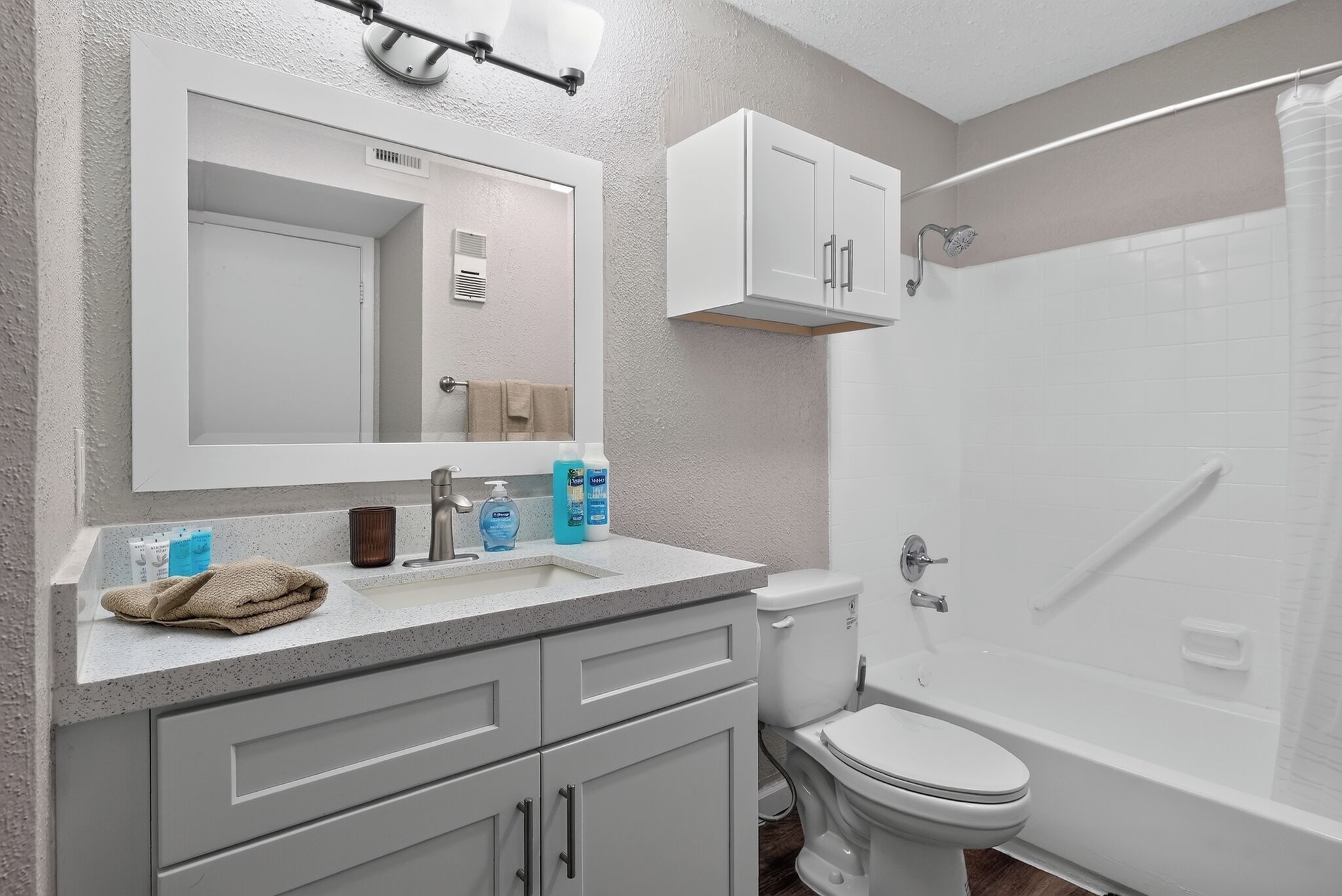 A bathroom with a white sink, mirror, and cabinet, a toilet, and a shower area.