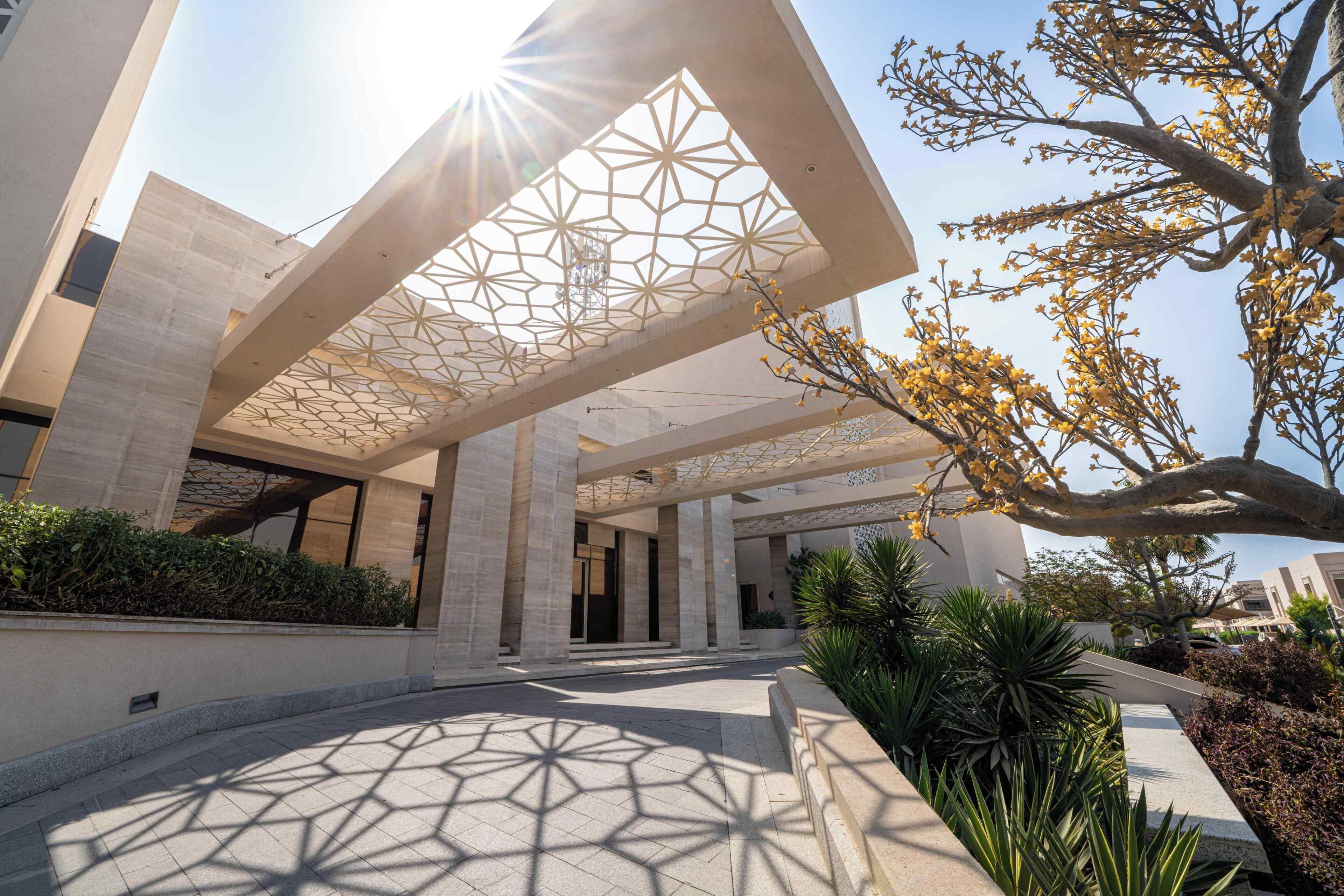 A modern building with a geometric patterned ceiling, large columns, and a paved walkway.