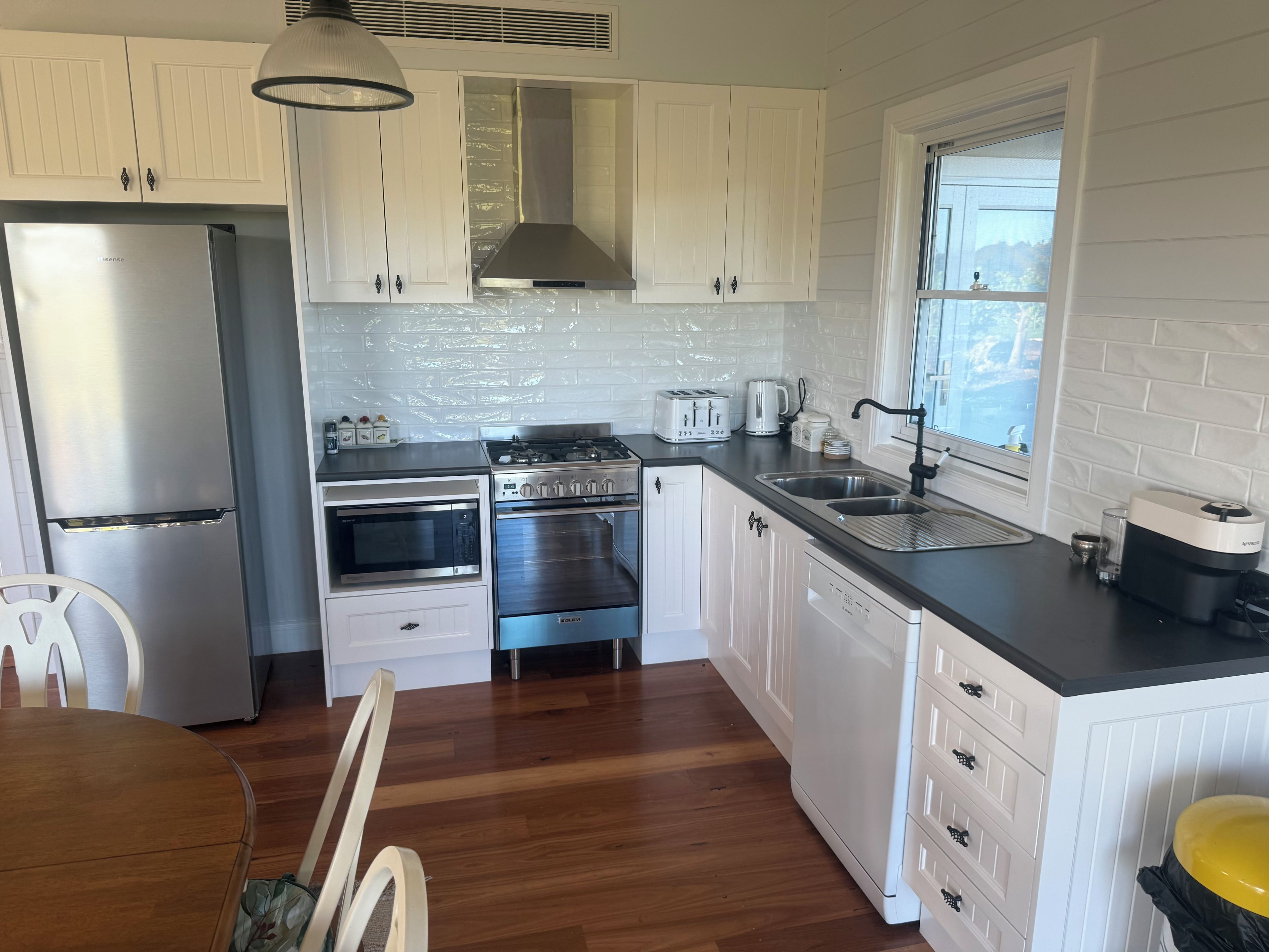 A modern kitchen with white cabinetry, stainless steel appliances, and a wooden dining table.