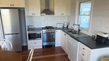 A modern kitchen with white cabinetry, stainless steel appliances, and a wooden dining table.