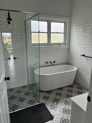 A modern bathroom with a freestanding bathtub, a glass shower enclosure, and patterned floor tiles.