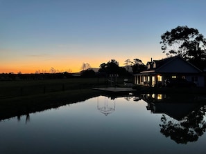 A house with a visible pond in front, a clear sky, and a sunset.