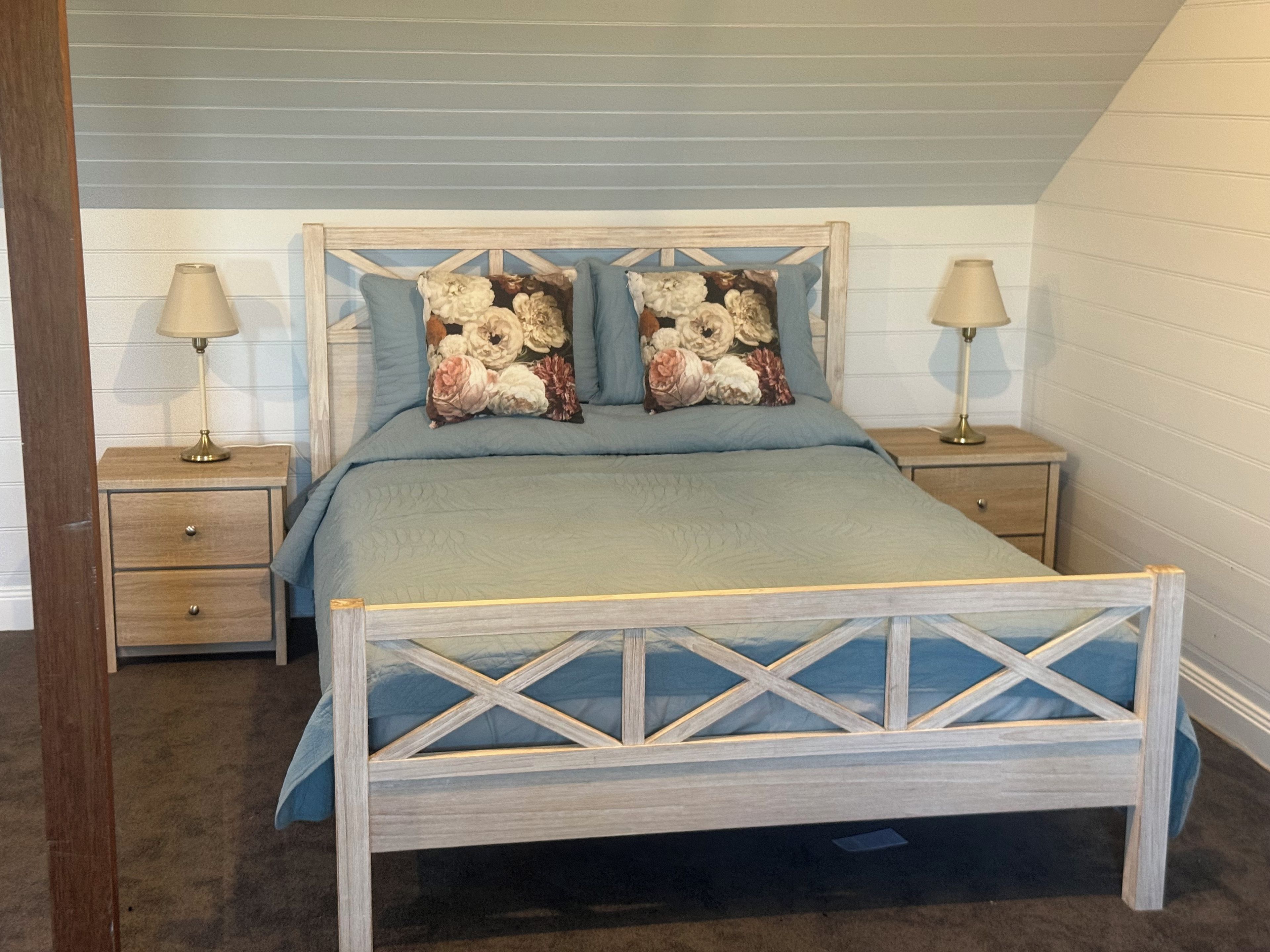 A bedroom with a wooden bed frame, two nightstands, a blue bedspread, and matching pillows.