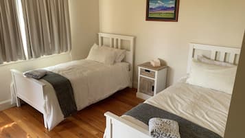 A bedroom with two beds, a bedside table with a tissue box, a painting on the wall, and a window with curtains.