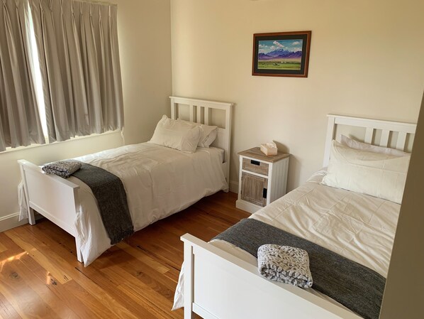 A bedroom with two beds, a bedside table with a tissue box, a painting on the wall, and a window with curtains.