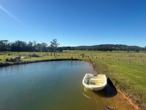 A small boat tied to a grassy bank of a calm water body, surrounded by a fenced field and trees in the background. - Lemongrove Cottage Berry Farm Stay (Berry)