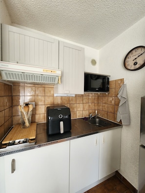 A kitchen with white cabinets, a microwave, a toaster, and a vintage clock on the wall. - Studio apartment with a pool, private parking space, and the ocean within walking distance (Bandol)