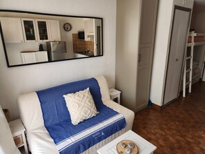 A living room with a sofa, a coffee table, and a mirror reflecting a kitchen area. - Studio apartment with a pool, private parking space, and the ocean within walking distance (Bandol)