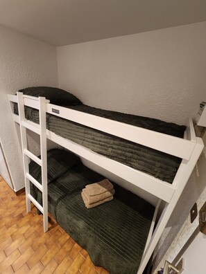 A bunk bed with a ladder, a green mattress, and a folded beige blanket. - Studio apartment with a pool, private parking space, and the ocean within walking distance (Bandol)
