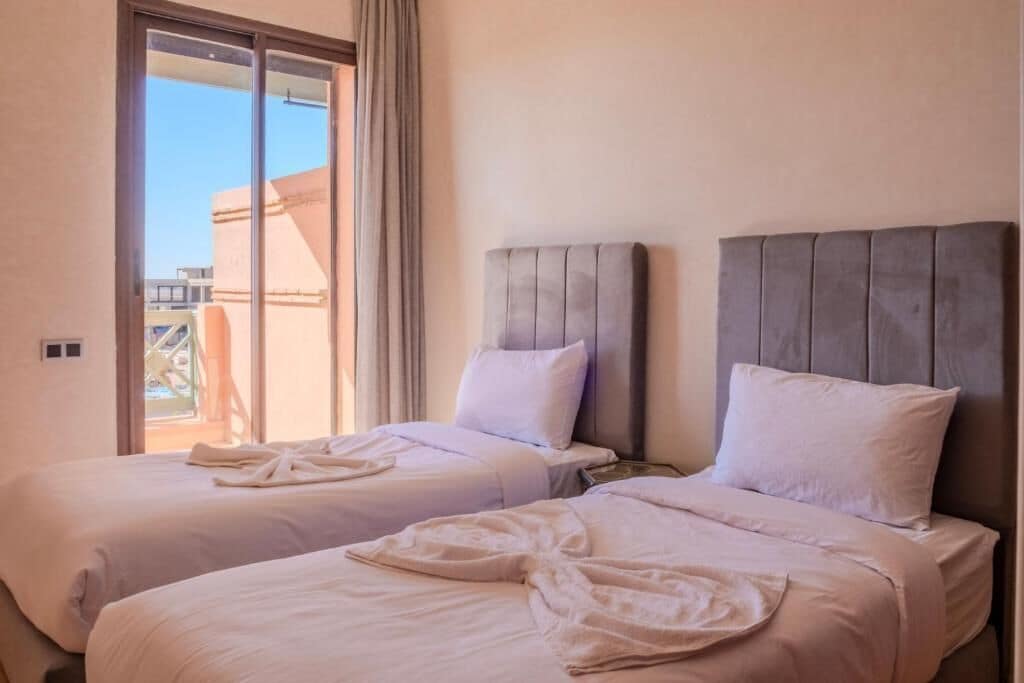 A hotel room with two beds, a large window, and a view of the outside.