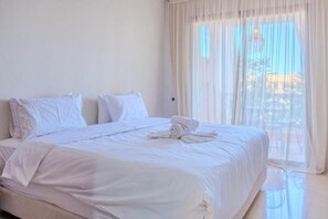 Una habitación de hotel con una cama grande, ropa de cama blanca y cortinas traslúcidas.
