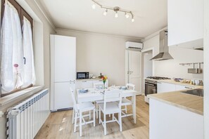 A compact kitchen with white cabinetry, a dining table with chairs, a built-in microwave, and a stove. - Rosa Olivi - Lavaiano (Lavaiano)