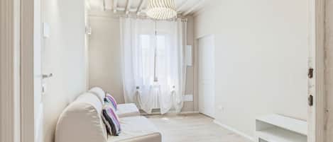 A spacious room with a white sofa, a ceiling light fixture, and a door leading to another room.