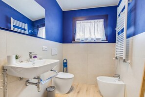 Un baño con un lavamanos grande, inodoro, bidé y una ventana con cortinas.