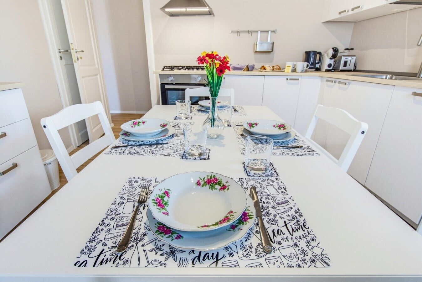 Une table à manger dressée pour quatre personnes, avec des nappes à motifs floraux et un vase rempli de fleurs.